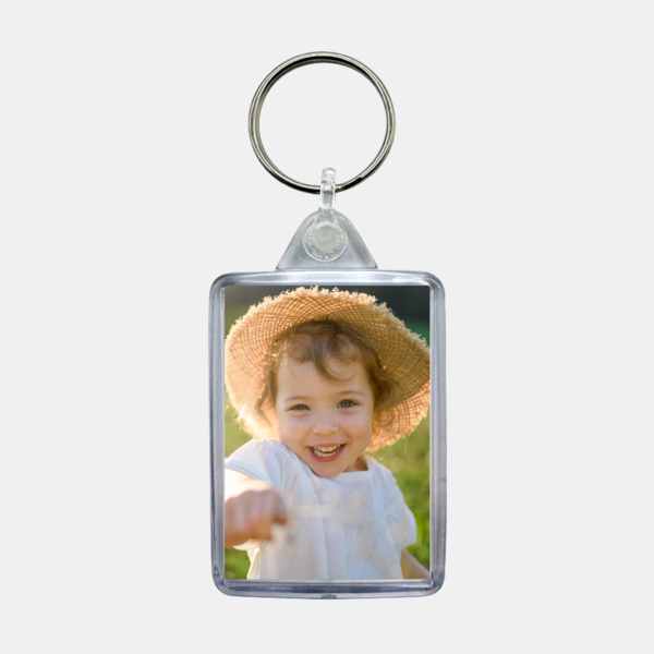 Der personalisierte Schlüsselanhänger zeigt ein fröhlich lachendes Kleinkind mit Strohhut auf einer Wiese im Sonnenlicht.