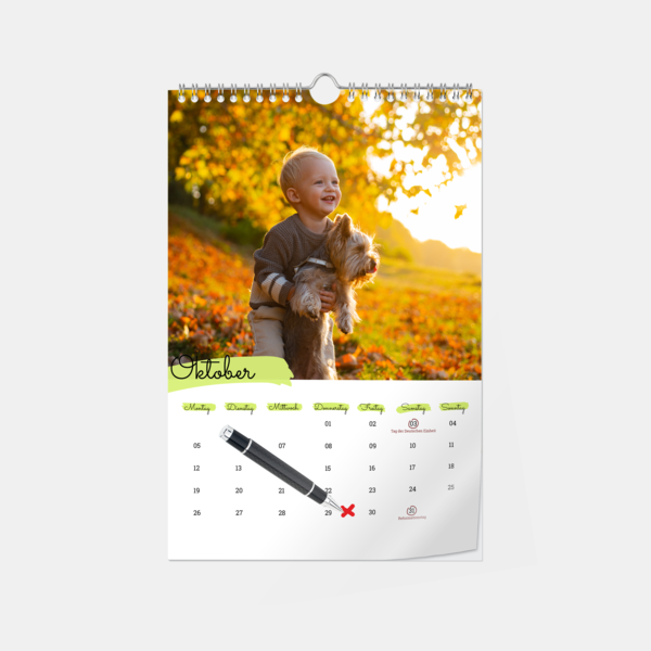Der Wandterminkalender zeigt einen lachenden Jungen mit Hund im Herbstlaub und ein markiertes Datum mit Kugelschreiber.