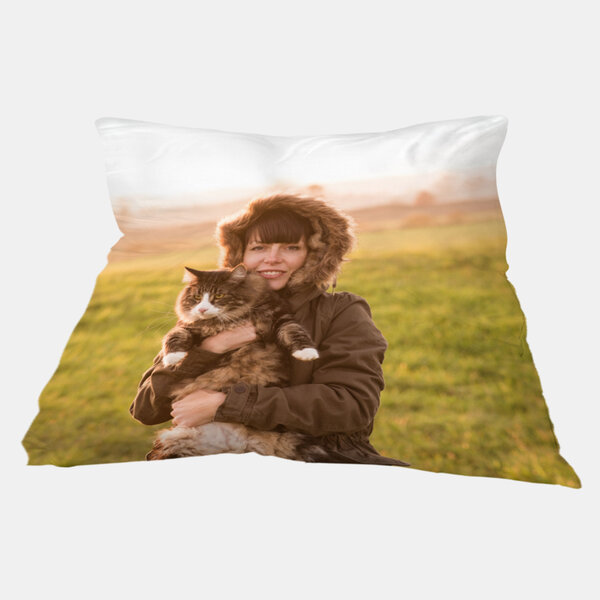 Ein personalisiertes Fotokissen zeigt eine Frau in Winterjacke, die bei Sonnenuntergang ihre Katze auf einer Wiese umarmt.